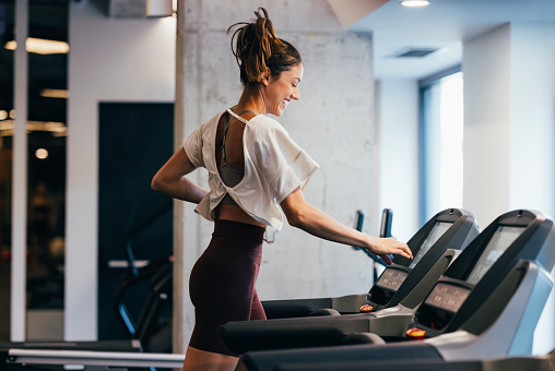 A motivated sportswoman setting the speed on a treadmill at the gym.