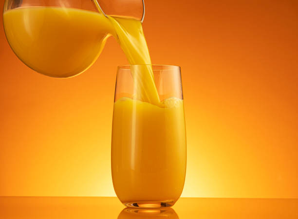 istock Orange juice pouring into glass with splash 1358140563