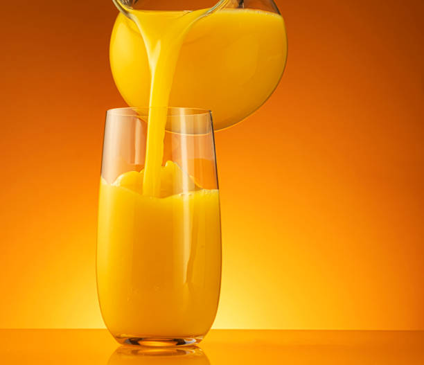 istock Orange juice pouring into glass with splash 1358140568