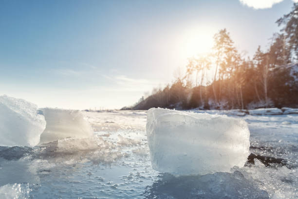 vue panoramique d’un morceau de tesson de glace clair sur la côte du paysage lacustre gelé contre les rayons chauds du soleil qui brillent à travers l’arbre de la forêt et le ciel bleu clair sur le fond. météo hivernale nature vue abstraite de la - tranquil scene tree sunset snow photos et images de collection