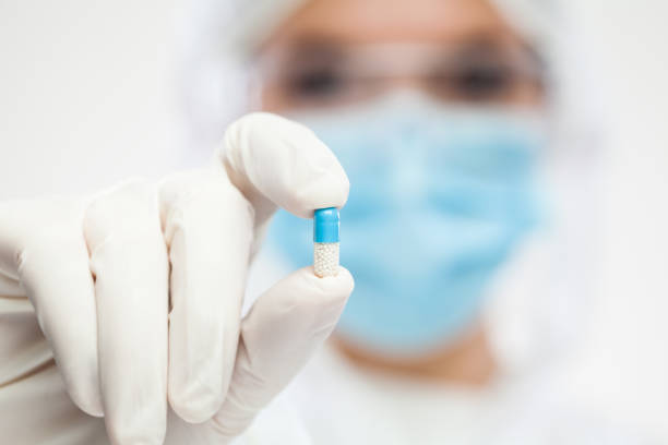 weibliche britische apothekerin trägt psa persönliche schutzausrüstung mit antibiotika-pille - surgical glove human hand holding capsule stock-fotos und bilder