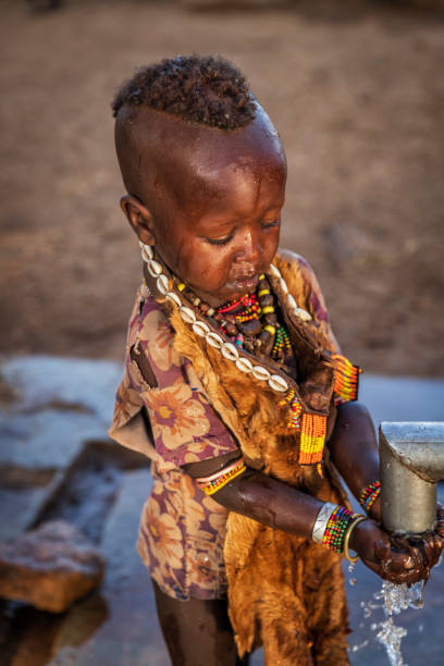 African little girl drinking water from hand water pump, Ethiopia, Africa African little girl drinking water from hand water pump. African women and children often walk long distances to bring back jugs of water that they carry on their back. hamer tribe photos stock pictures, royalty-free photos & images