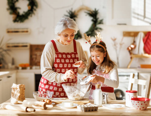 süßes kleines mädchen, das der älteren großmutter hilft, teig für traditionelle weihnachtsplätzchen zu machen - grandmother cooking baking family stock-fotos und bilder