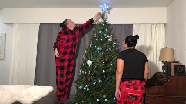 A woman putting up the star on top of the tree