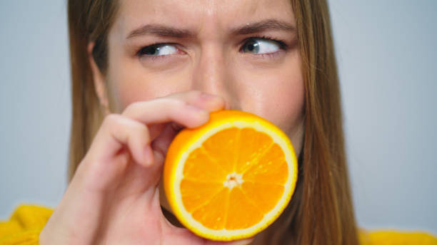 istock Closeup positive woman making funny faces with orange in hands in studio. 1358146829