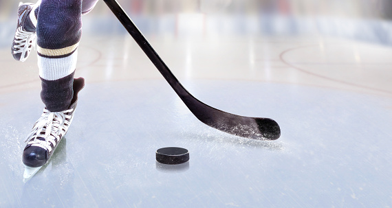 Low angle view of ice hockey player with stick on ice rink controlling puck and copy space.