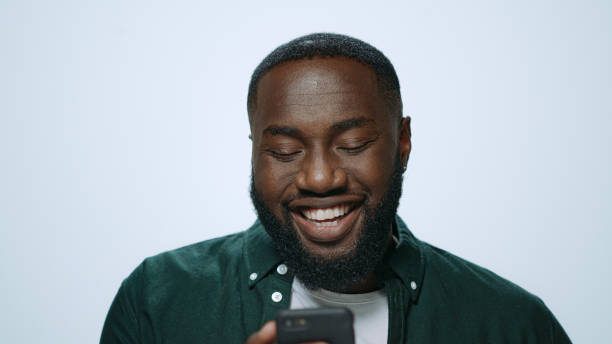 istock Closeup happy african man browsing internet online on mobile phone in studio. 1358153522