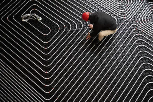 Installing heating system in building. Worker adjusting position of pipes. Diagonally oriented pattern on tubes. Construction of modern family house.