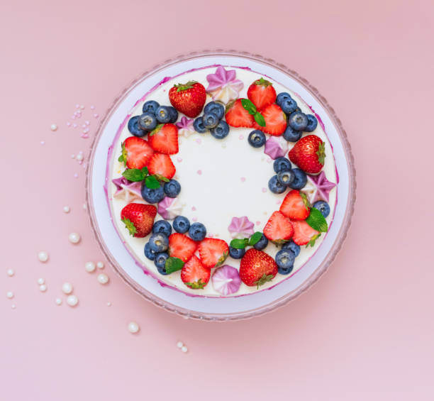 istock Delicate cake garnished with fresh strawberries blueberries on a pink plain background. Festive dessert with berries 1358161243