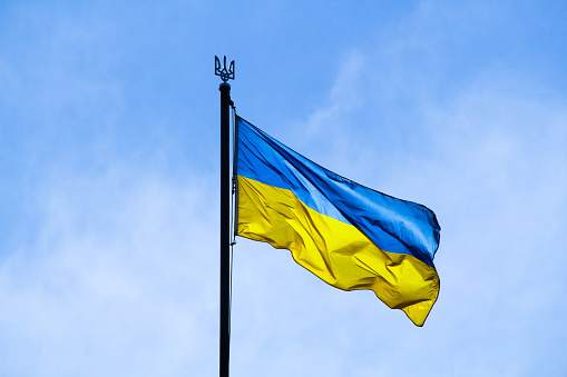 Ukrainian flag in the rays of the rising sun on a background of sky. Bicolor blue and yellow national flag of Ukraine on a flagpole and coat of arms of Ukraine trident. Official symbol of Ukraine