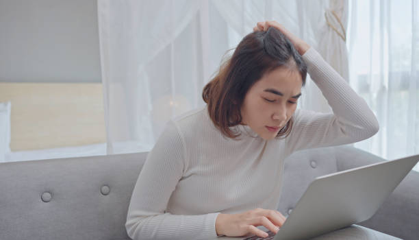 istock Stressed young woman holding head in hands and looking at laptop screen, having problems with project, sitting on sofa in living room. 1358163837