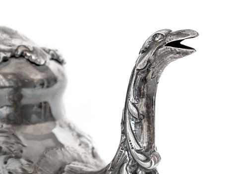 Antique sterling silver tea pot. Spout is a creature with open mouth; possible snake or dragon. Repousse tea pot body. Sterling silver. Isolated on white.