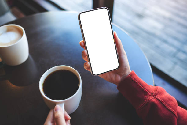 istock Mockup image of a woman holding mobile phone with blank white screen while drinking coffee in cafe 1358170845
