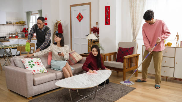 istock lazy asian mother playing with phone on sofa and giving command with hand gestures while other family memebers cleaning house for chinese new year. translation: spring and congratulations everyone 1358179022