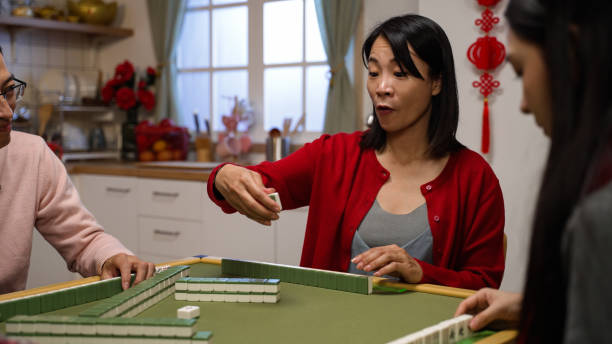 istock selective focus of smiling mother drawing keeping a tile and discarding another from her hand while playing mahjong game at home with family on chinese lunar new year's eve 1358179325