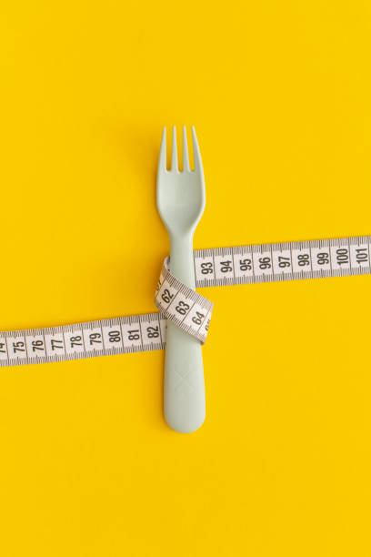 istock Measuring tape and fork on yellow background. Weight loss concept 1358183369
