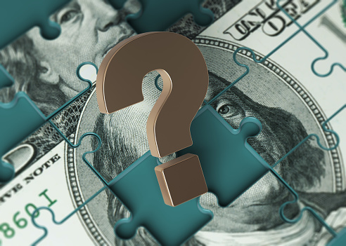 Puzzle-shaped 100 American dollar banknote and gold-colored question mark symbol. On a charcoal green-colored background. Horizontal composition with copy space. Isolated with clipping path.