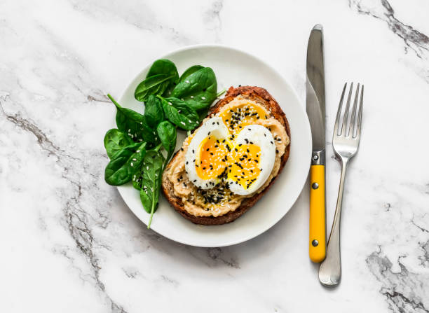 istock Whole grain grilled bread hummus, boiled egg, sesame sandwich and fresh spinach on a light background, top view 1358184387