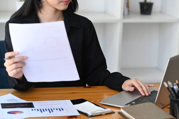 istock Businesswoman holding paperwork and working with laptop computer. 1358184502