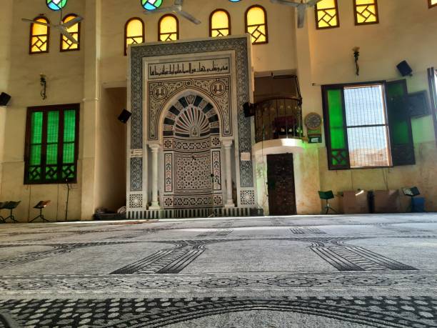 un interior de mezquita, una mezquita desde el interior a la luz del día con alfombras, ventanas de colores y un mihrab - alquibla fotos fotografías e imágenes de stock