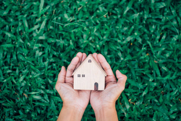 istock Hand hold house model on green grass background 1358188258