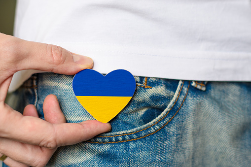 Patriot of Ukraine! Wooden badge with the flag of Ukraine in the shape of a heart in a man's hand. National holiday of Ukraine