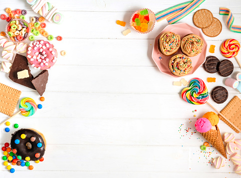 Kids party background with sweet food - donuts, cookies, chocolate bars, lollipops, marshmallows and marmalade. White wooden backdrop with blank space for text. Top view, flat lay.