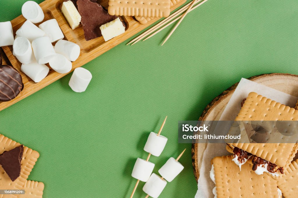 S'mores roasting marshmallows with chocolate between cookies S'mores roasting marshmallows with chocolate between cookies on green background with blank space for text. Top view, flat lay. Camping Stock Photo