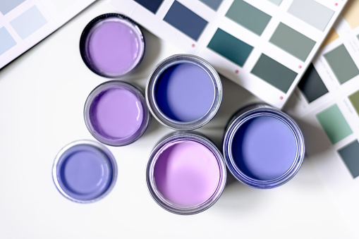 Tiny sample paint cans during house renovation, process of choosing paint for the walls, violet very peri color of the year 2022, color charts on background