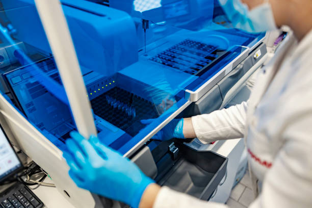istock Microbiology and modern technology in lab. A scientist with sterile gloves is standing next to a machine for blood analyzing and putting test tubes with blood samples in it. 1358201256