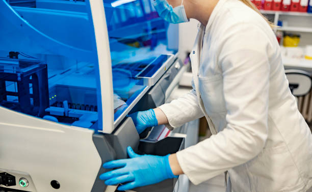 istock Blood samples analysis. A nurse with sterile gloves and mask is standing next to a machine for blood sampling and putting test tubes in it. Microbiology and medicine. 1358202770