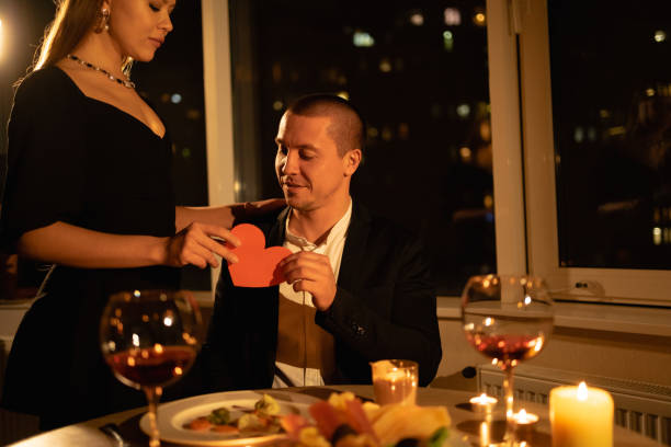 istock Romantic dinner for Valentine's Day for two, a date with a candle with wine in the evening, a couple in love, a girl giving a man a heart 1358205019