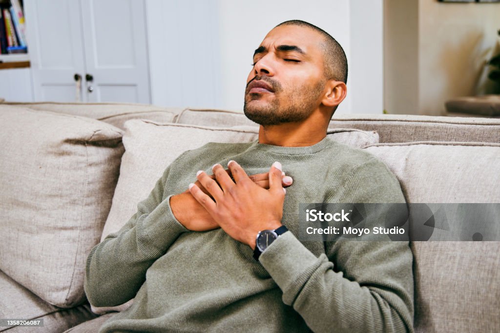 Shot of a young man experiencing chest pains at home Someone call the hospital Breathing Exercise Stock Photo