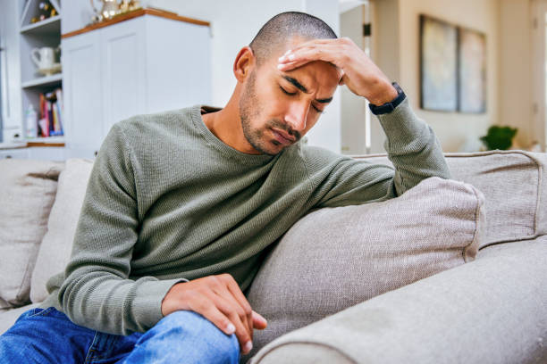 Shot of a young man experiencing a headache while relaxing at home stock photo