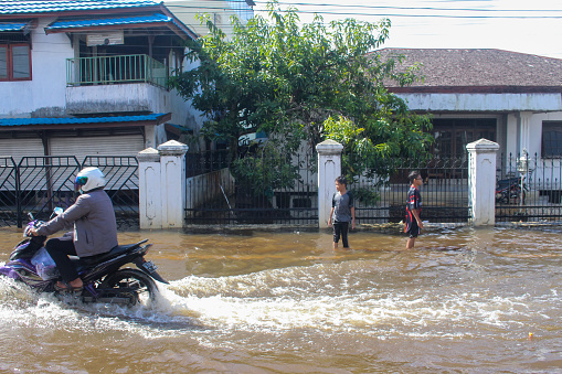 Banjarmasin, Indonesia - December 9, 2021: Banjarmasin residents use cars, motorbikes to walk across the flooding street in Sultan Adam, Banjarmasin, Indonesia.