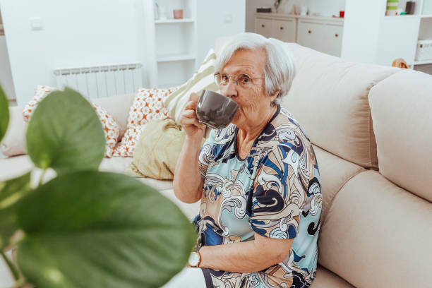 elderly woman drinking coffee sitting on couch - 96 well imagens e fotografias de stock