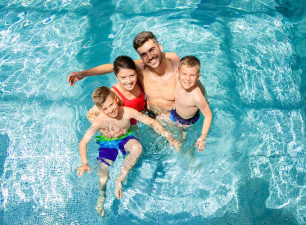 top-blick auf lächelnde vierköpfige familie, die spaß hat und sich im hallenbad im hotelresort entspannt. - swimmingpool stock-fotos und bilder