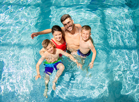 Vista superior de la sonriente familia de cuatro personas divirtiéndose y relajándose en la piscina cubierta del complejo hotelero. photo