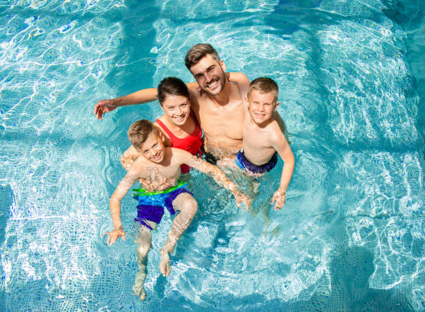 vue de dessus d’une famille souriante de quatre personnes s’amusant et se relaxant dans la piscine intérieure du complexe hôtelier. - bassin photos et images de collection