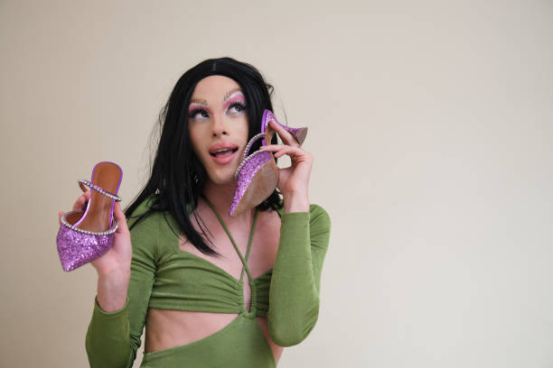 Portrait of a drag queen person posing holding heels on beige background. Portrait of a drag queen person wearing a green dress posing holding purple heels on beige background. crossdressing shoes stock pictures, royalty-free photos & images