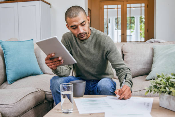 Shot of a man filling out paperwork while using his digital tablet Making a day of admin exciting filling out stock pictures, royalty-free photos & images