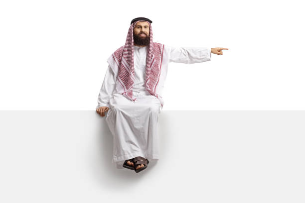 istock Saudi arab man sitting on a blank panel and pointing 1358214690