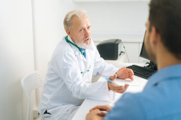 istock View from back to gray-haired senior physician in medical coat explaining problem to unrecognizable male patient during consultation at hospital. 1358214713