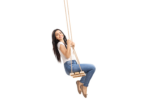 Side shot of a young brunette swinging on a wooden swing and looking at the camera isolated on white background
