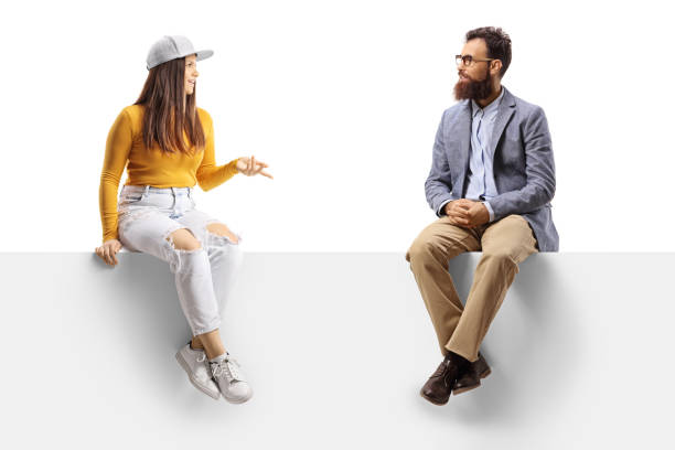 istock Teen female and a bearded man sitting on a blank panel and having a conversation 1358214739