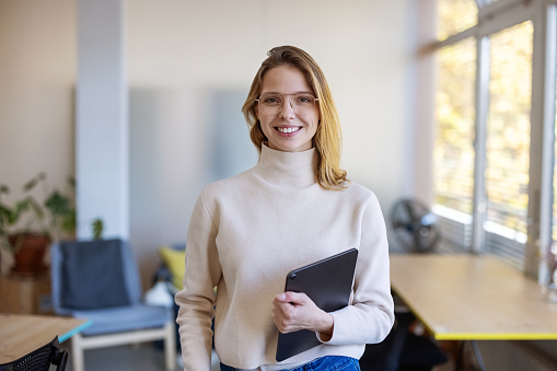 Portrait of a successful businesswoman standing at startup company. Female executive holding digital tablet looking at camera.