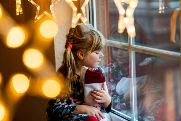 Little preschool girl holding cup Santa Claus boot with gift called Nikolausstiefel in German. Happy child wait on holiday by window with Christmas lights in winter. Cozy family celebration of xmas. stock photo
