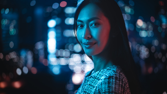 Hermoso retrato femenino asiático de pie en City Street con luces de neón a altas horas de la noche. Auténtica mujer adulta segura de sí misma posando para la cámara, sonriendo en la noche en el centro de Business Street. photo