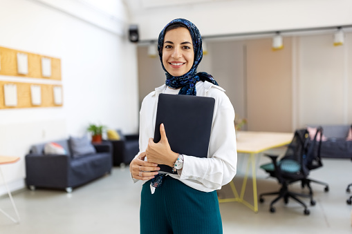 Portrait of a middle eastern businesswoman at office. Woman executive wearing headscarf smiling at camera holding a file.