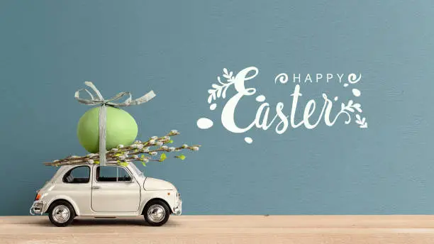 Photo of Retro car carrying an Easter egg on the roof. Happy Easter text